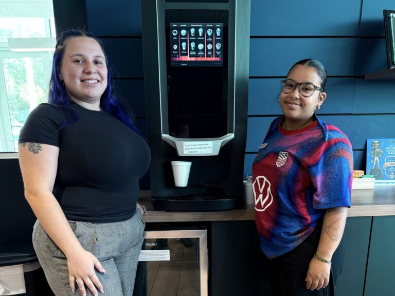 Two team members standing beside a bean-to-cup breakroom coffee machine installed at a Central Florida facility